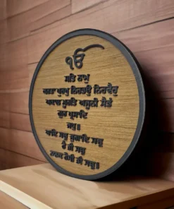 Round wooden plaque with engraved Sikh religious text in Punjabi, mounted on a wooden wall.